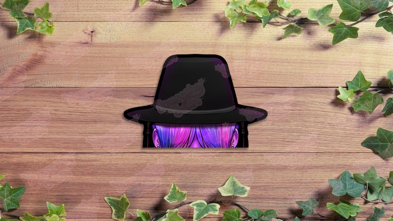 May include: A black fedora hat with a decorative design, partially obscuring a glimpse of purple and pink hair. The hat is set against a wooden background, with green leaves in the corners.