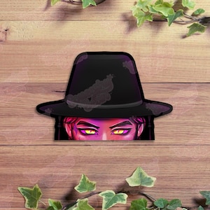 May include: A sticker featuring a black fedora hat with a purple outline and a face with yellow eyes peeking out from underneath. The sticker is set against a wooden background with green ivy.