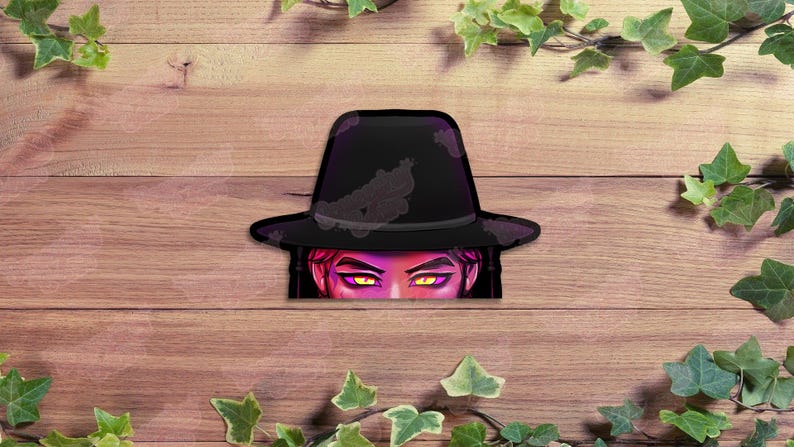 May include: A sticker featuring a black fedora hat with a purple outline and a face with yellow eyes peeking out from underneath. The sticker is set against a wooden background with green ivy.