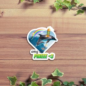 May include: A sticker featuring a dolphin leaping from ocean waves under a rainbow. The dolphin is holding a bottle of something. The sticker has the text "omg da PINEEE <3" in a heart-shaped design.
