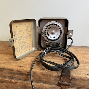 May include: A silver Tork Time Switch No. 919 (1) with a round dial and a black cord. The dial has markings for "Night", "Evening", "Afternoon", and "Morning".