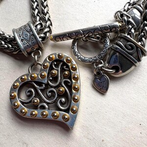 Pu&ograve; includere: Collana color argento con un ciondolo a forma di cuore. Il ciondolo presenta una cornice argentata con accenti dorati e un design traforato. La collana ha una chiusura a toggle e un piccolo ciondolo a forma di cuore. La catena &egrave; a treccia.