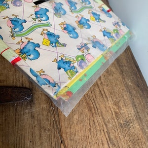 May include: A pack of blue bird themed wrapping paper. The paper features a repeating pattern of blue birds wearing party hats, balloons, and gifts. The paper is wrapped in clear plastic.