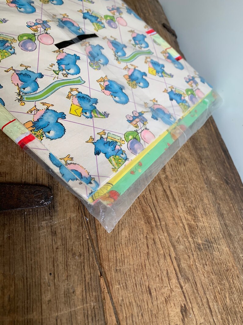 May include: A pack of blue bird themed wrapping paper. The paper features a repeating pattern of blue birds wearing party hats, balloons, and gifts. The paper is wrapped in clear plastic.
