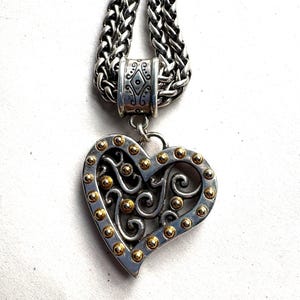 Pu&ograve; includere: Collana con pendente a forma di cuore argentato e dettagli dorati. Il cuore presenta un design traforato ed &egrave; impreziosito da piccole sfere dorate sui bordi. La catena &egrave; argentata.
