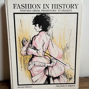 May include: A book titled "Fashion in History: Western Dress, Prehistoric to Present" with a second edition copyright. The cover features a black and white illustration of a woman wearing a pink dress with a large bustle.