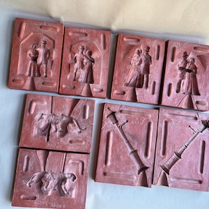 May include: A collection of eight reddish-brown plaster molds. The molds depict various scenes, including couples in period clothing, a horse and rider, and a street lamp. The molds are rectangular and appear to be vintage.