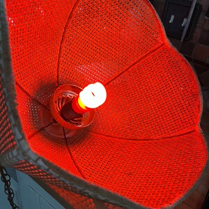Puede incluir: Una pantalla de l&aacute;mpara naranja tejida con una bombilla en su interior. La pantalla est&aacute; hecha de un material tejido y tiene una forma redonda.