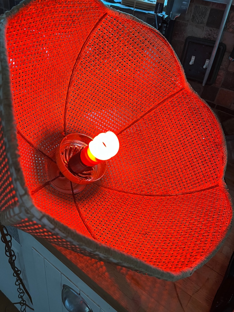 Puede incluir: Una pantalla de l&aacute;mpara naranja tejida con una bombilla en su interior. La pantalla est&aacute; hecha de un material tejido y tiene una forma redonda.