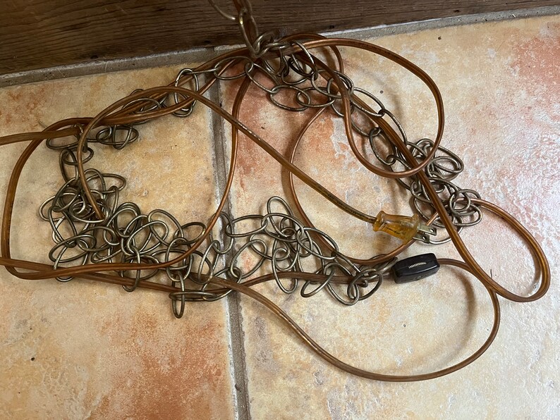 Puede incluir: Primer plano de un cable el&eacute;ctrico marr&oacute;n con una cadena plateada unida. El cable est&aacute; enrollado y enredado, y la cadena est&aacute; suelta y colgando.