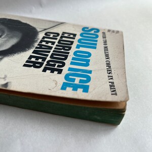 May include: A paperback book titled "Soul on Ice" by Eldridge Cleaver. The cover features a black and white photo of a man with a beard and afro. The book cover is white with blue and black text. The text "Over two million copies in print" is printed on the cover.