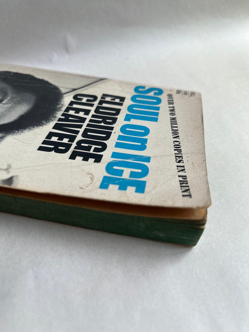 May include: A paperback book titled "Soul on Ice" by Eldridge Cleaver. The cover features a black and white photo of a man with a beard and afro. The book cover is white with blue and black text. The text "Over two million copies in print" is printed on the cover.