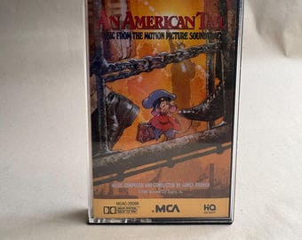 May include: A vintage cassette tape for the soundtrack of "An American Tail." The cover features a cartoon mouse in a hat and a suitcase, with the title text in red and the film's title. The tape is in a black case.
