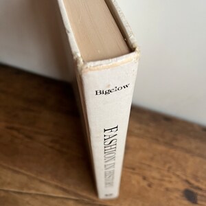 May include: A white book with the title "Fashion in History" by Bigelow on the spine.