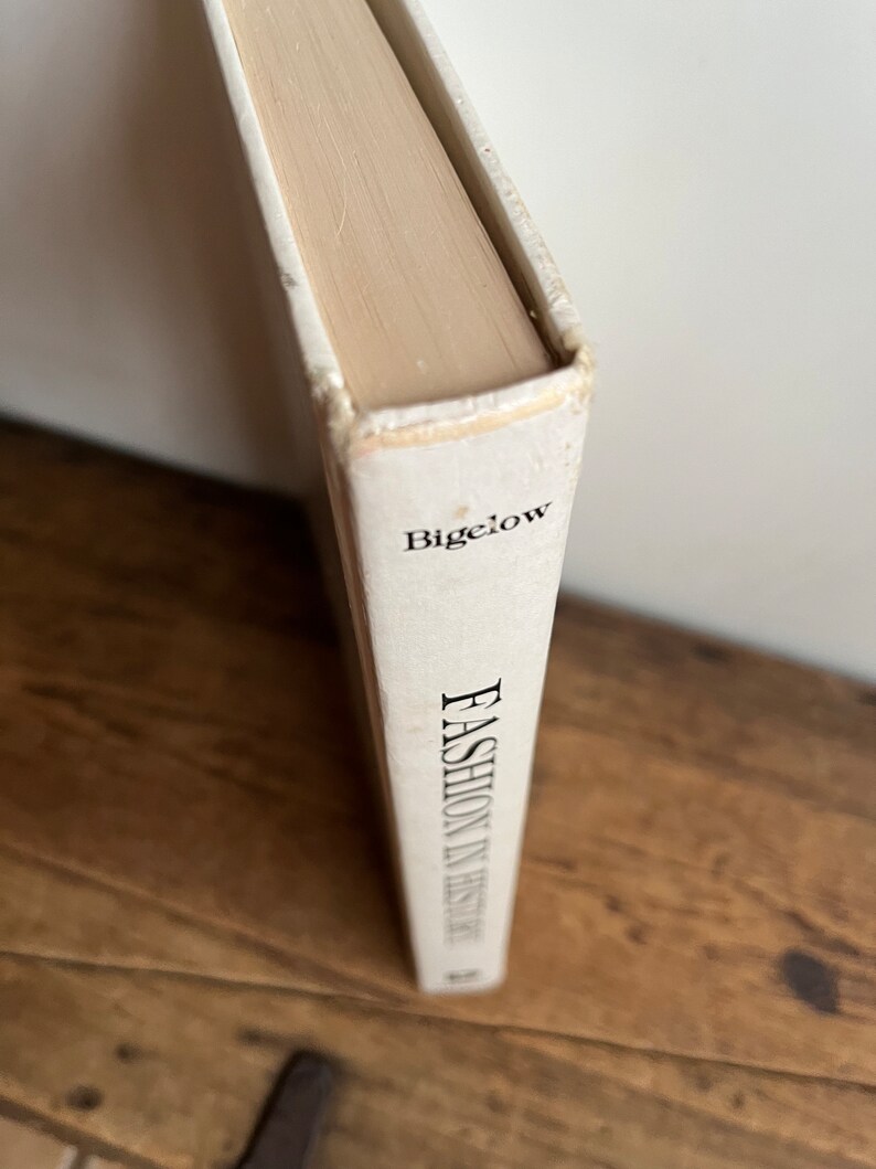 May include: A white book with the title "Fashion in History" by Bigelow on the spine.