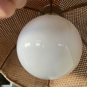 Puede incluir: Una l&aacute;mpara de globo blanco con una pantalla de mimbre tejido. La pantalla es marr&oacute;n y tiene un borde festoneado.