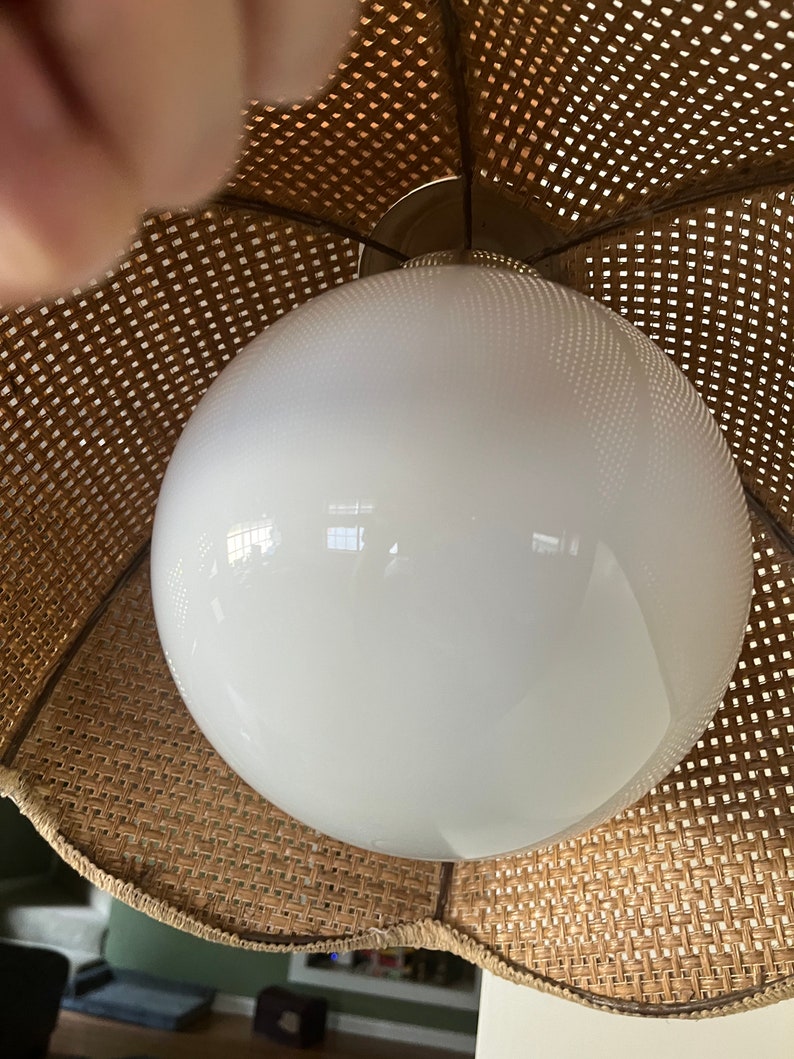 Puede incluir: Una l&aacute;mpara de globo blanco con una pantalla de mimbre tejido. La pantalla es marr&oacute;n y tiene un borde festoneado.