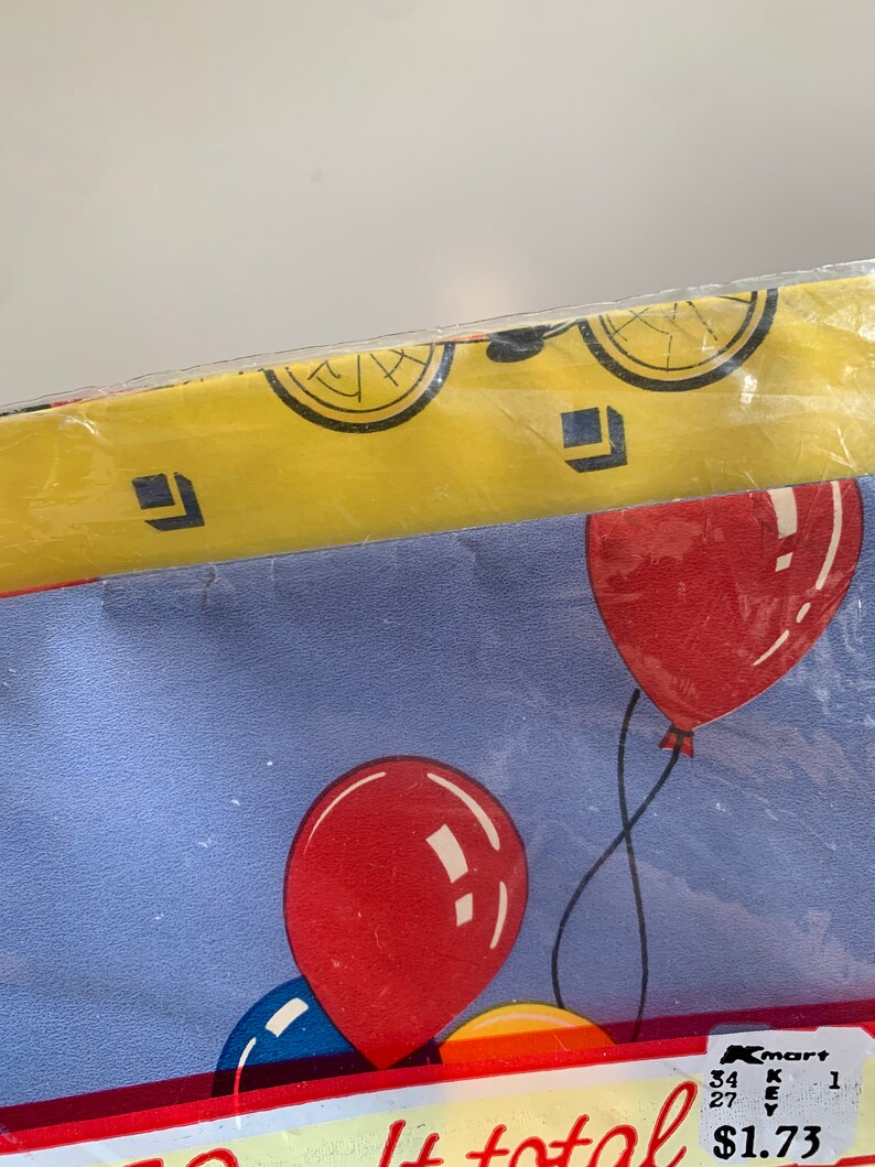May include: A blue and yellow tablecloth with a red, blue, and yellow balloon pattern. The tablecloth has a Kmart price tag that says "&pound;1.73".
