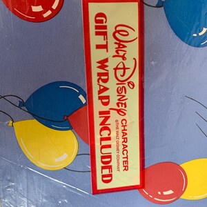 May include: Blue wrapping paper with a red border and a red and white label that says "Walt Disney Character Gift Wrap Included" with a copyright symbol and "The Walt Disney Company". The paper is decorated with colourful balloons.