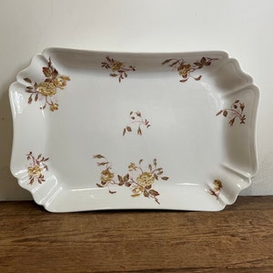 May include: A white porcelain serving tray with a scalloped edge and a floral design in shades of brown and yellow.
