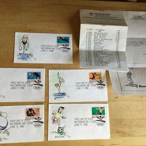 May include: A set of nine envelopes with stamps commemorating the 1992 Summer Olympics in Barcelona, Spain. Each envelope features a different Olympic sport, including volleyball, boxing, soccer, and gymnastics. The envelopes are white with black and red ink drawings of athletes competing in each sport. The stamps are all the same, featuring the Olympic rings and the words "First Day of Issue" and "Baltimore MD 21233".