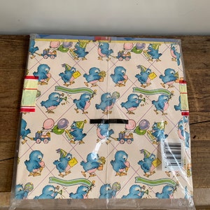 May include: A pack of blue bird themed wrapping paper with a white background. The birds are wearing party hats and holding gifts, balloons, and flowers. The paper is wrapped in clear plastic.
