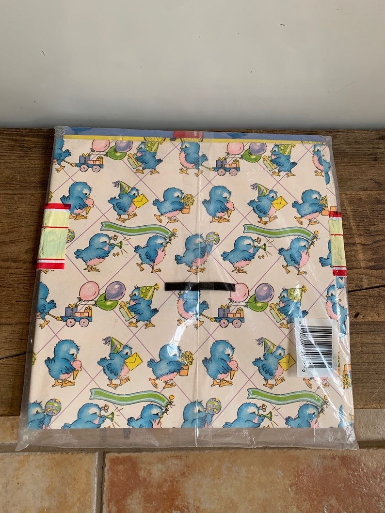 May include: A pack of blue bird themed wrapping paper with a white background. The birds are wearing party hats and holding gifts, balloons, and flowers. The paper is wrapped in clear plastic.