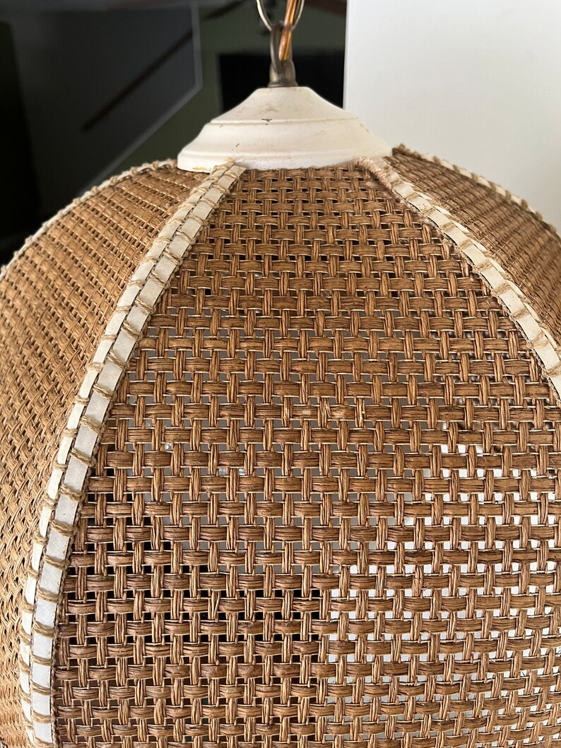Puede incluir: Una l&aacute;mpara colgante de mimbre tejido con una parte superior blanca y un borde blanco alrededor del borde. La l&aacute;mpara est&aacute; hecha de materiales naturales y tiene un estilo r&uacute;stico y de granja.