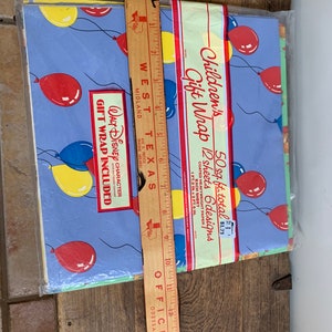 May include: A pack of 12 sheets of Children's Gift Wrap featuring a blue background with red, yellow, and blue balloons. The pack states that it contains 50 square feet of gift wrap and is priced at &pound;1.73. The text "WALT DISNEY CHARACTER GIFT WRAP INCLUDED" is printed on the pack.