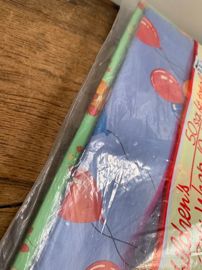 May include: A pack of wrapping paper with a blue background and red balloons. The text on the pack says "50 sq ft.  Birthday Wrap".