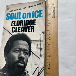 May include: A vintage paperback book cover with a black and white photo of a man with a beard. The title of the book is "Soul on Ice" by Eldridge Cleaver. The cover is blue, white, and black.