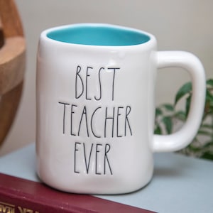 Puede incluir: Taza de cerámica blanca con interior azul turquesa. La taza tiene texto negro que dice "BEST TEACHER EVER".