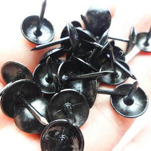 May include: A pile of black upholstery tacks with round heads and sharp points.