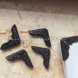 Op de afbeelding: Vijf zwarte metalen hoekbeschermers met een decoratief ontwerp. Elke beschermer meet 20 mm bij 14 mm.