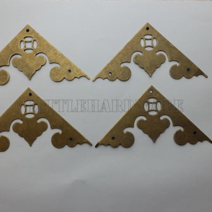 Puede incluir: Cuatro escuadras de esquina antiguas de latón con diseños decorativos recortados y orificios de montaje. Se incluye un pequeño montón de tornillos a juego. Las escuadras son triangulares y presentan un patrón floral estilizado.