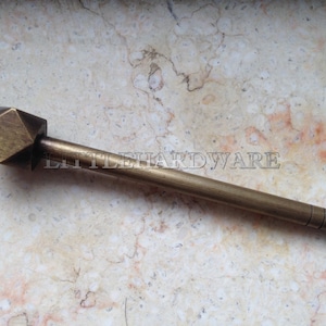 Peut inclure: Un pêne de porte en laiton avec une tête hexagonale et un long fût fin. Le pêne a une rainure décorative près de l'extrémité du fût.