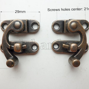 May include: Two antique bronze-colored latches. Each latch measures 33mm in height and 29mm in width. The screw hole center distance is 21mm. The latches have a curved hook design and are suitable for small boxes or chests.