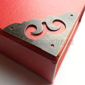 May include: A close-up of a red box with a decorative metal corner piece. The corner piece is a swirling design with a distressed finish.