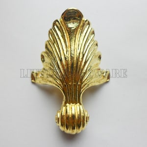 Puede incluir: Pata de mueble de metal dorado con un diseño decorativo en forma de abanico. La pata tiene una base redonda y estriada.