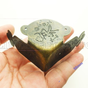 Könnte beinhalten: Eckwinkel in antikem Messingfarbton mit floralem und Vogeldesign. Die Halterung ist 5,8 cm breit, 3,5 cm hoch und 2,5 cm tief. Sie hat eine dekorative, Vintage-Ästhetik, geeignet für Bastel- oder Möbelrestaurierungsprojekte.