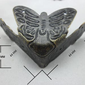 Puede incluir: Escuadra de esquina de metal bronce antiguo con diseño de mariposa. La escuadra mide 4,4 cm por cada lado y 2 cm de alto. El motivo decorativo de mariposa está diseñado para proteger y embellecer esquinas.
