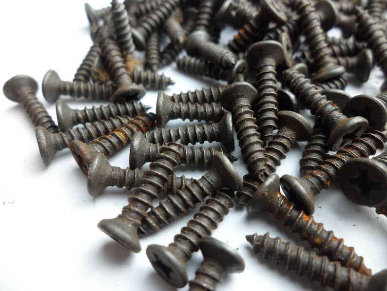 May include: A pile of black screws with a rusty finish. The screws are scattered on a white surface.