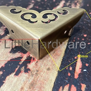May include: Brass corner bracket with a decorative design. The bracket is 5 cm wide and 12.5 cm long.