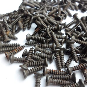 May include: A large pile of black screws with a rusty finish. The screws are scattered on a white surface.
