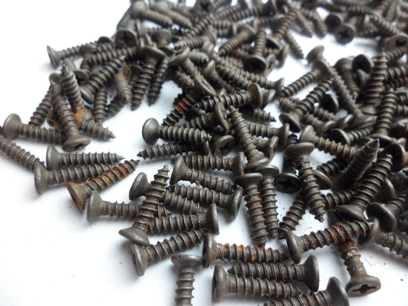 May include: A large pile of black screws with a rusty finish. The screws are scattered on a white surface.
