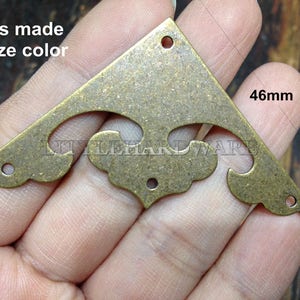 Könnte beinhalten: Eine Eckkonsole aus Messing mit einem dekorativen Design, in Bronzefarbe. Die Konsole ist 46 mm lang.