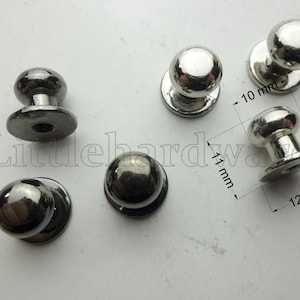 May include: Six shiny, silver-colored cabinet knobs with a rounded top and a flat base. The knobs are approximately 10 mm to 12 mm in size. The knobs are displayed on a light-colored surface.