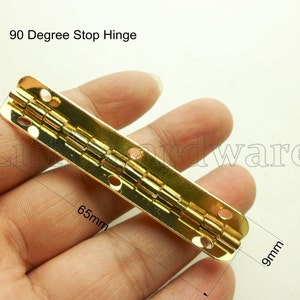 Può includere: Una cerniera di arresto a 90 gradi di colore dorato che misura 16,5 cm di lunghezza e 0,9 cm di larghezza. La cerniera ha più fori per viti ed è progettata per fermarsi a un angolo di 90 gradi.
