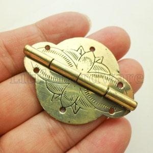 Puede incluir: Una bisagra de metal dorado con un diseño floral decorativo. La bisagra está cerrada y tiene un pasador en forma de barril.