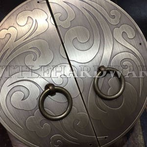 May include: A pair of antique brass door pulls with intricate swirling designs. The pulls have a brushed finish and are attached to a wooden door.